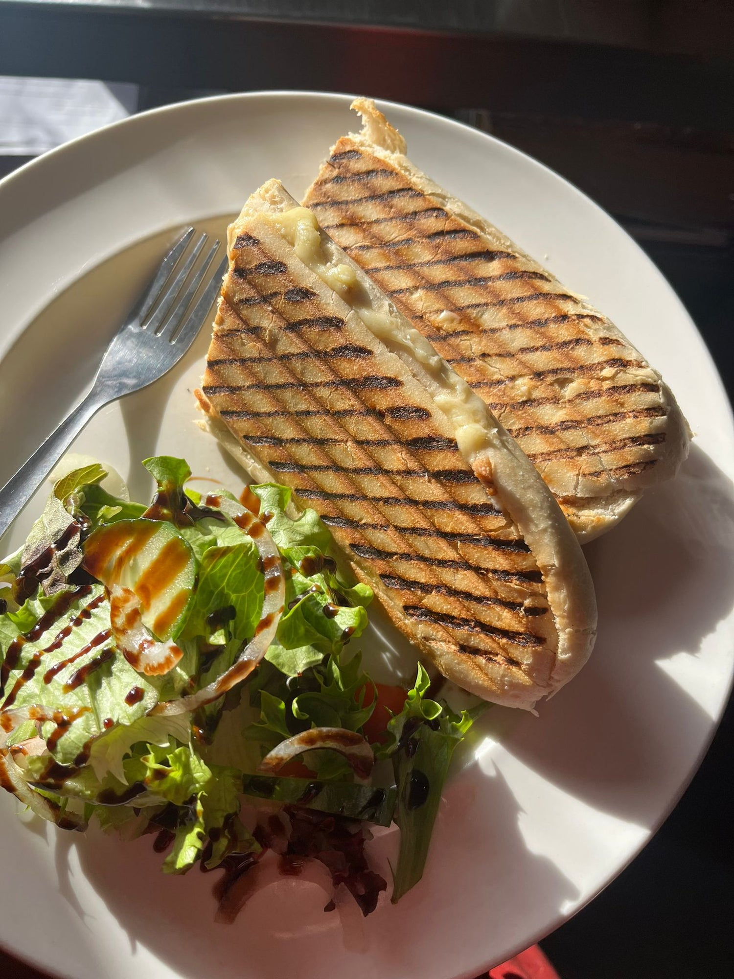 Grilled sandwich on a white plate with a side of salad and a fork.