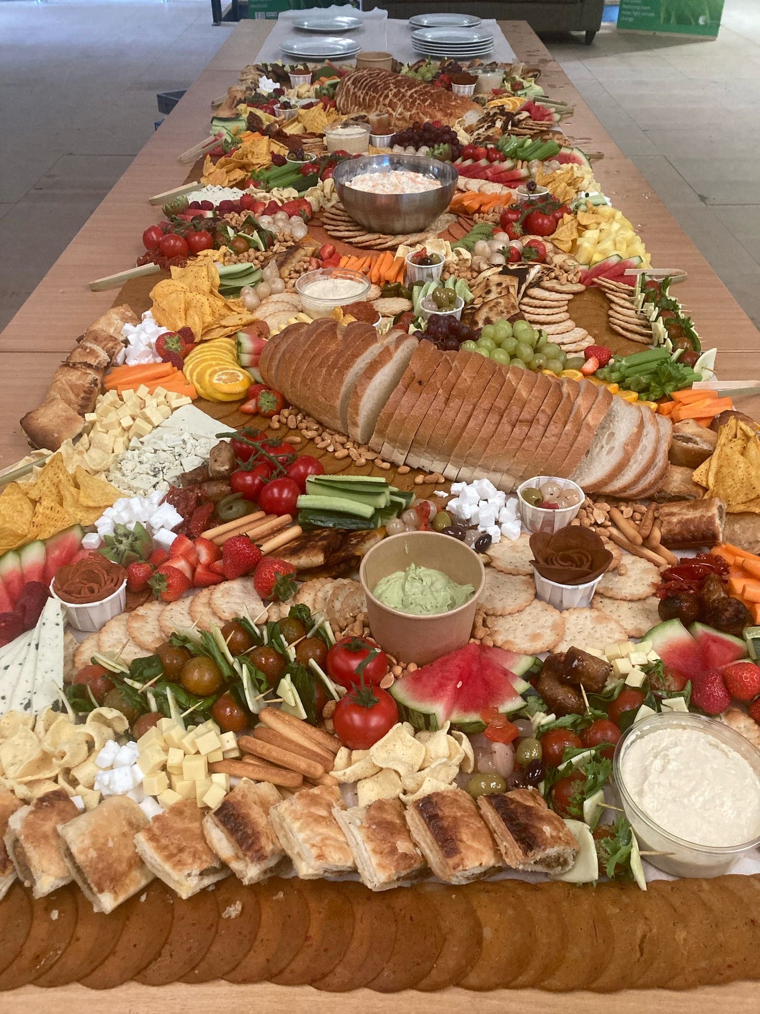 Large platter of assorted finger foods including bread, vegetables, and dips on a wooden table.